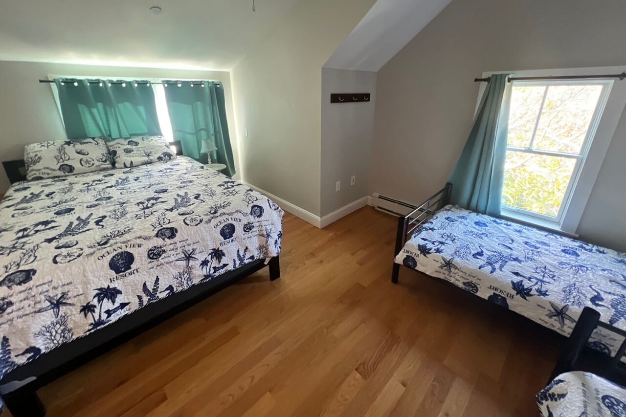 a large room with wood floors, large windows, one queen bed, and two twin beds