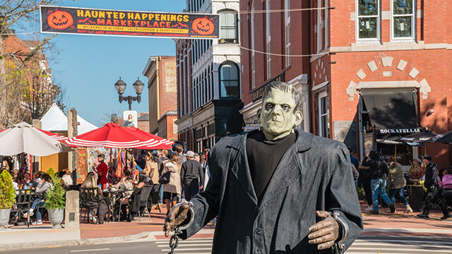 a Frankenstein's monster figure in front of the brick buildings of Salem, MA with a "Haunted Happenings" banner above.