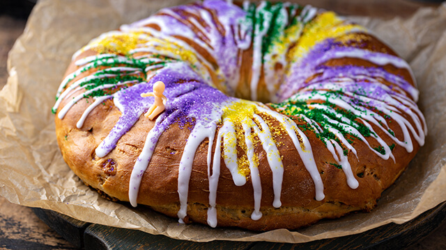 a circular shaped cake with purple, green, yellow, and white icing and sprinkles