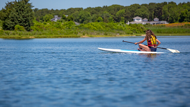 a woman sits on a stand-up paddle board in the middle of a pond on Martha's Vineyard, MA