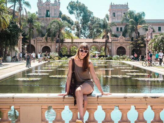 a young woman in sunglasses poses at Balboa Park in the sunshine