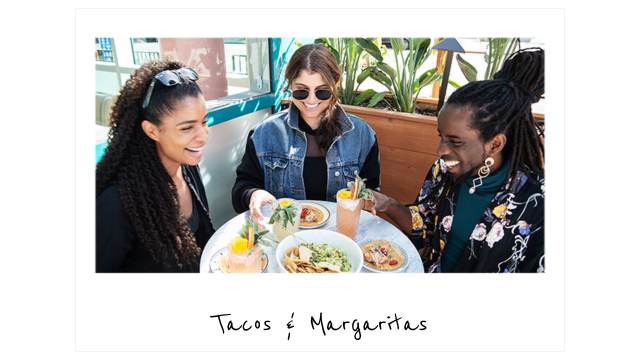 a group of three young friends sits around a table laughing over tacos and margaritas