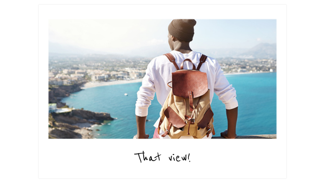 a traveler in a white t-shirt and dark brown knit cap wearing a leather backpack sits on a wood railing overlooking a body of water