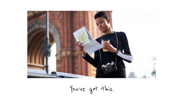 a young traveler stands in front of a brick arch looking at a paper map and holding a cup of coffee