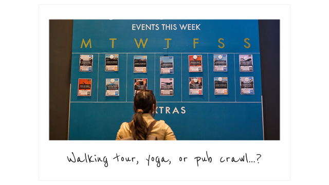 a woman seen from behind looking at a colorful events calendar on a blue wall at a HI USA hostel