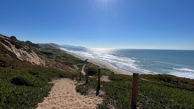 A path leads down green cliffs to the beach at Fort Funston in San Francisco.