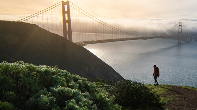 a hiker in the Marin Headlands stands overlooking the golden gate bridge at sunset