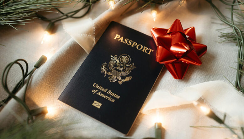 a dark blue US passport with a red bow on it sits under a Christmas treet