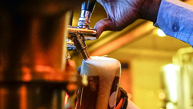 A hand pours a frothy beer from a tap into a glass beer stein